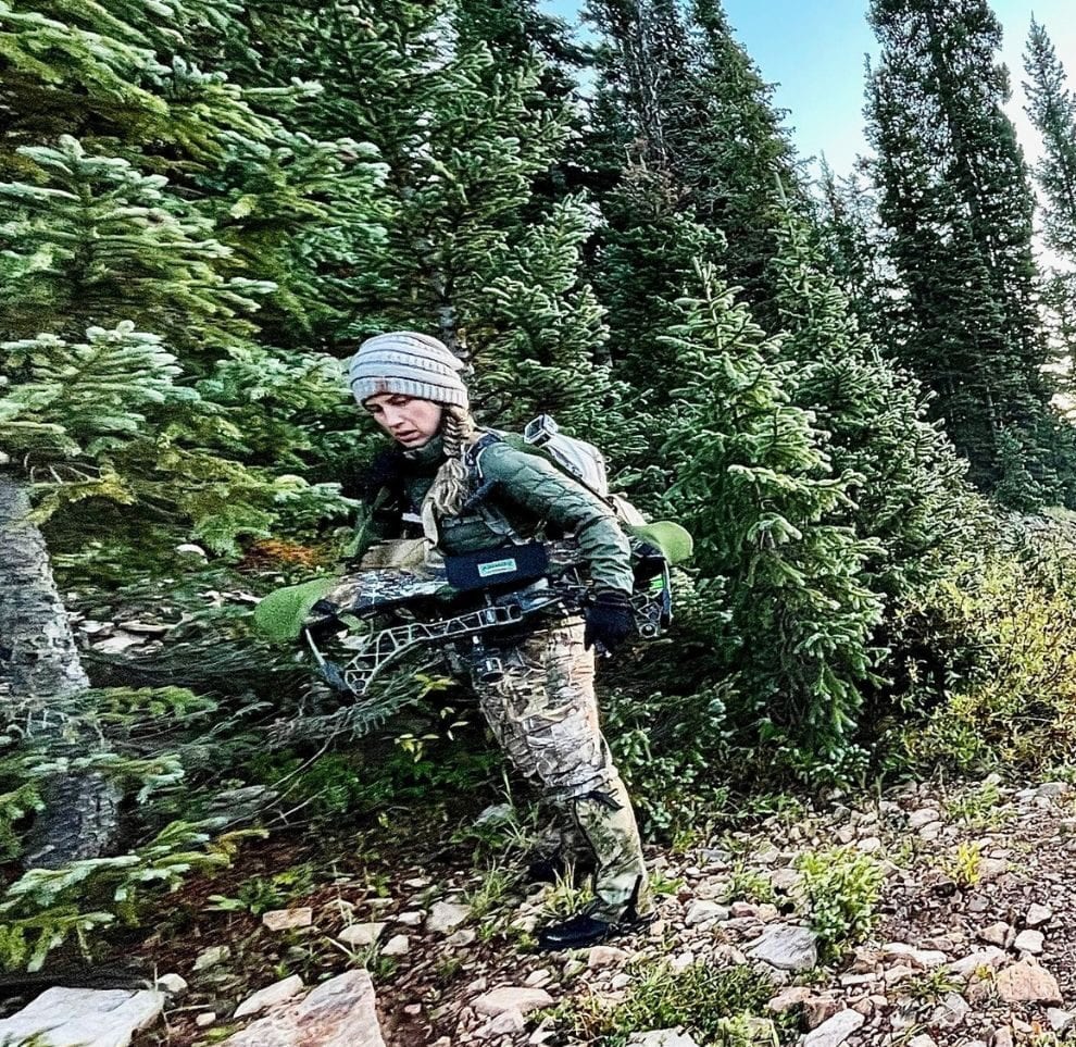 Bowhunter in camo moving through evergreen forest in the San Juans