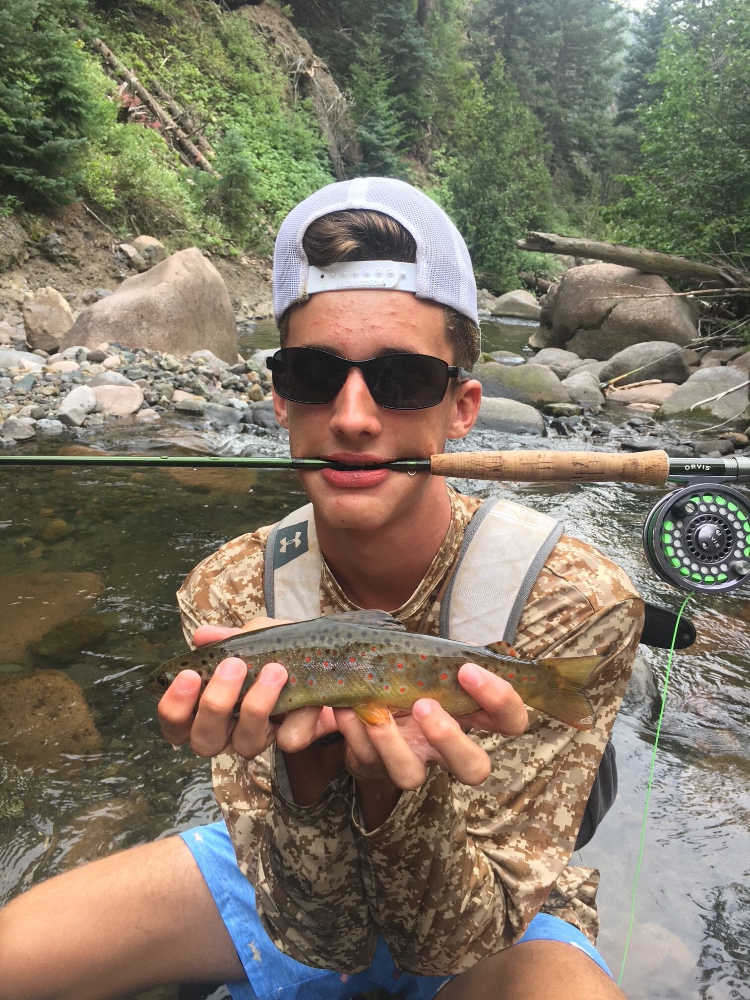 Angler holding a brown trout with fly rod on a boulder-lined river