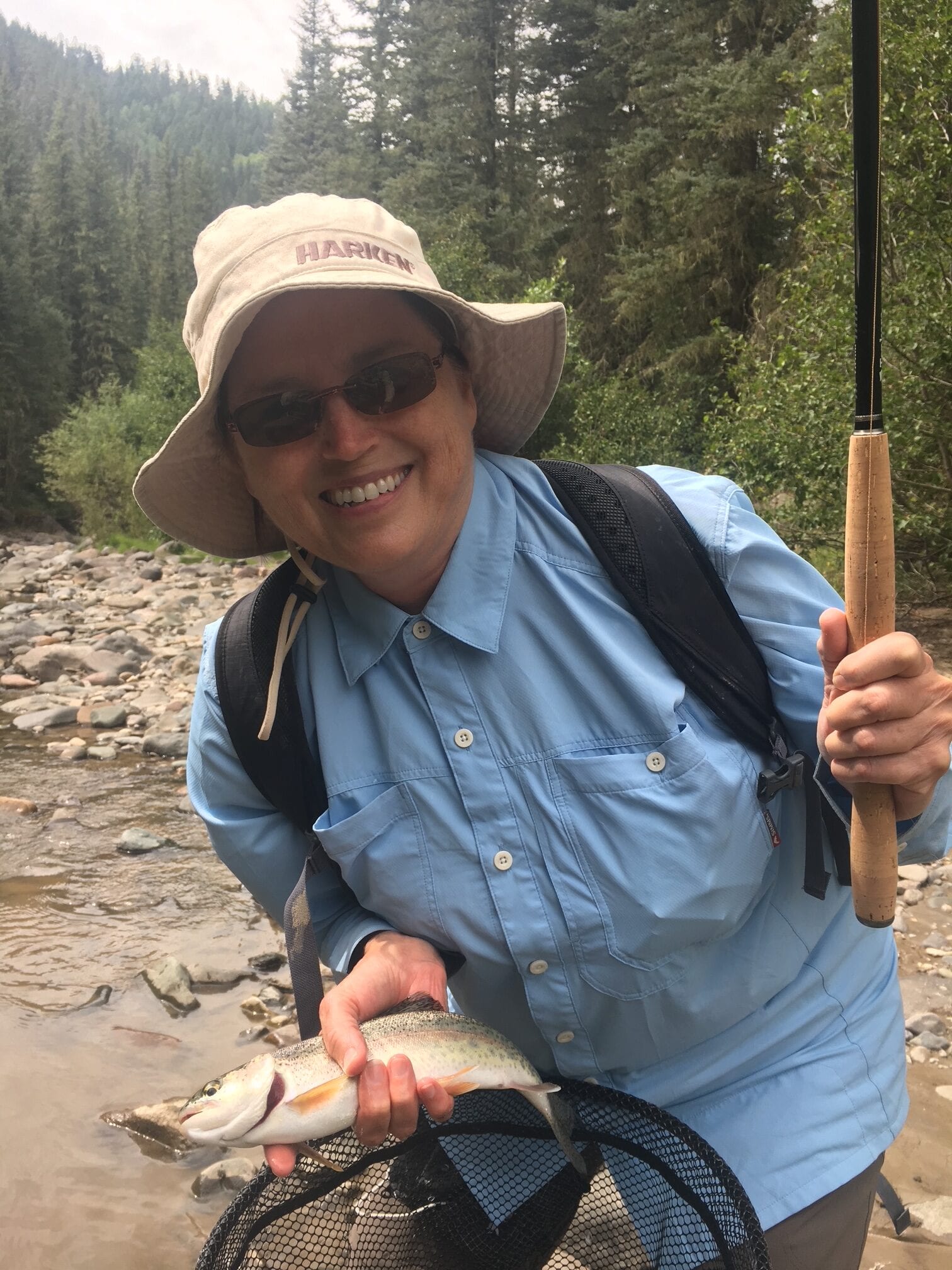 Angler with a wild trout on a forested river in the Rio Grande National Forest